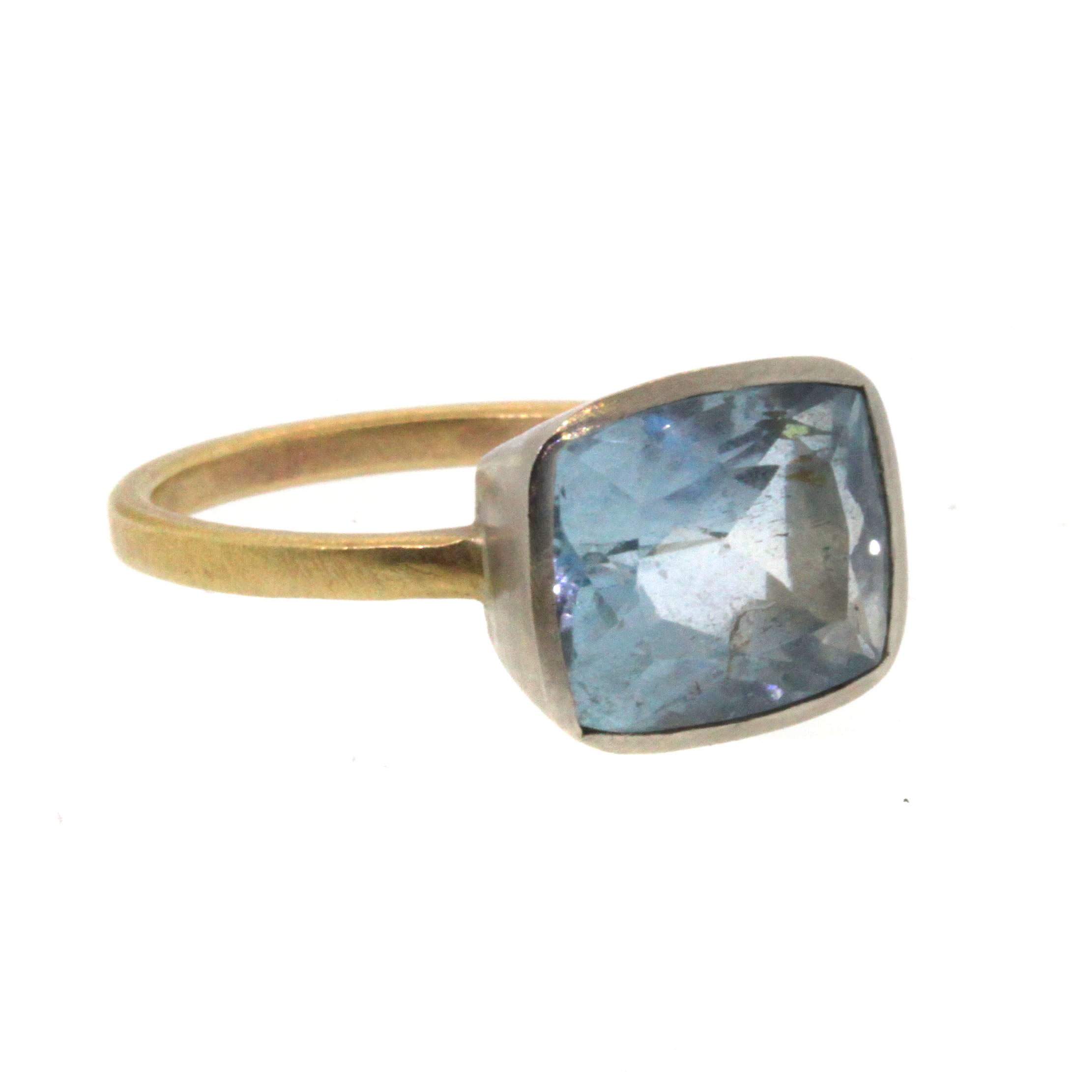 This Cushion Aquamarine Ring was handcrafted by Rebecca Lankford. It features a brilliant, blue aquamarine bezel set in white gold and soldered into a textured yellow gold band. 