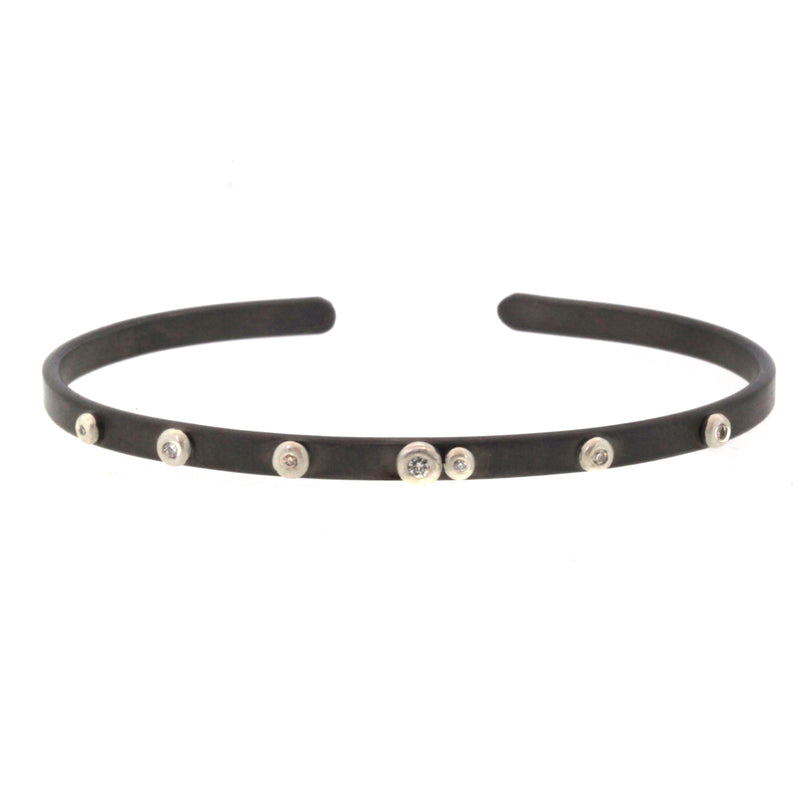 This Scattered Diamond Cuff Bracelet was handcrafted by Rebecca Lankford in Houston Heights. It features 7 diamond bezel set in sterling silver and scattered onto a thin rhodium plated cuff.